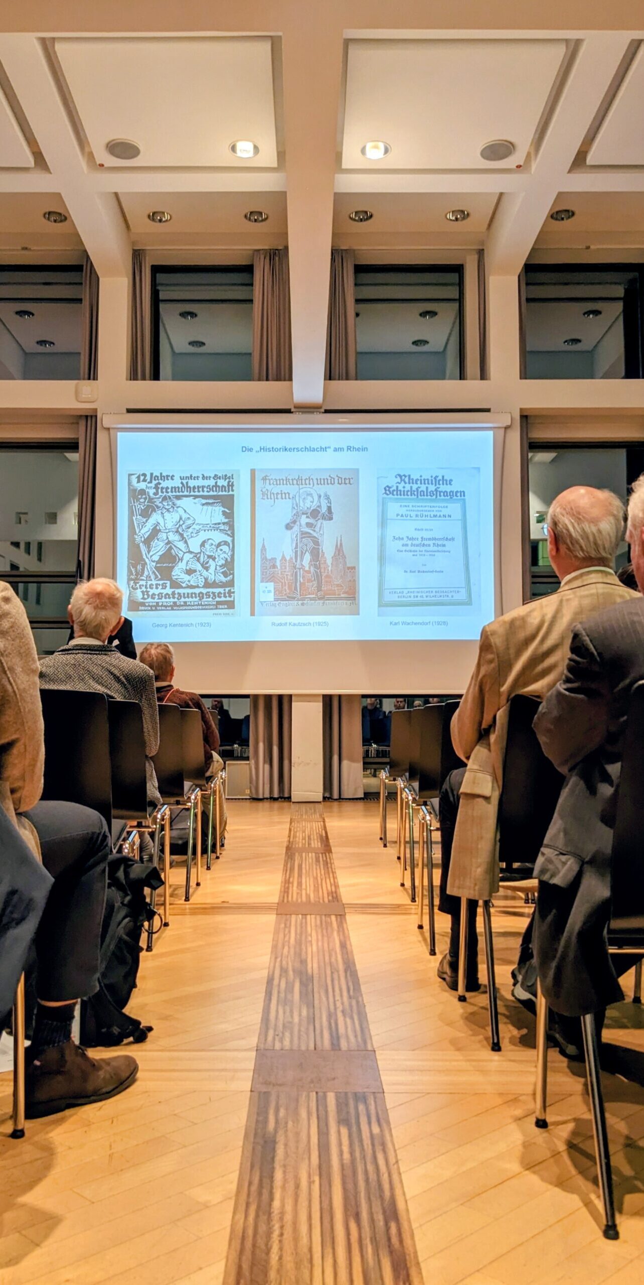 Blick durch Stuhlreihe auf Leinwand mit Vortragsbildern.